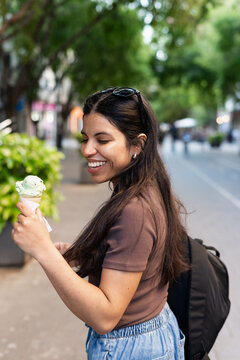 Young Woman Enjoys Ice Cream While Walking in City Street