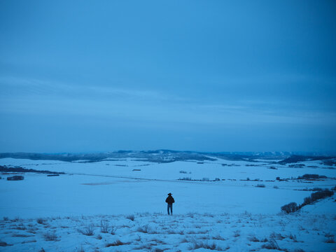 Lone Figure Walking on Snowy Landscape in Winter at Dusk