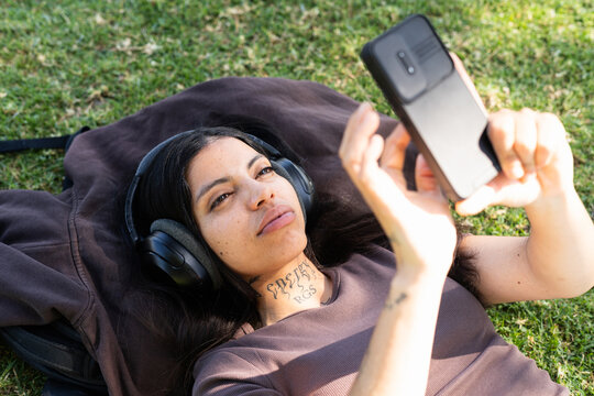 A woman listens to music and uses a phone while lying on the grass
