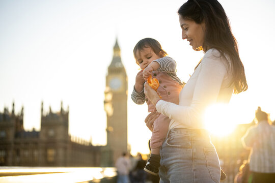 Mother Sharing A Snack With Toddler Near Big Ben At Sunset