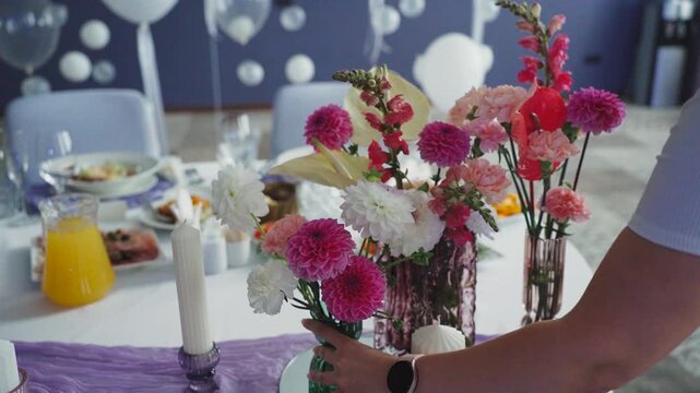 Decorator places flower on festive table. Floral decoration of banquet hall. Arrangement of vibrant seasonal flowers creates romantic atmosphere, perfect for weddings, dining events, celebrations.
