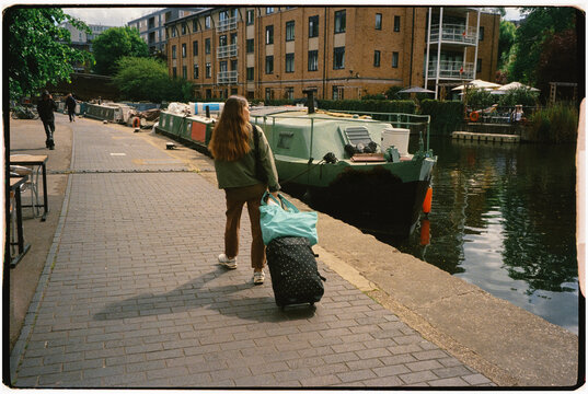 Woman walks on a canal path in London, pulling suitcase with wheels