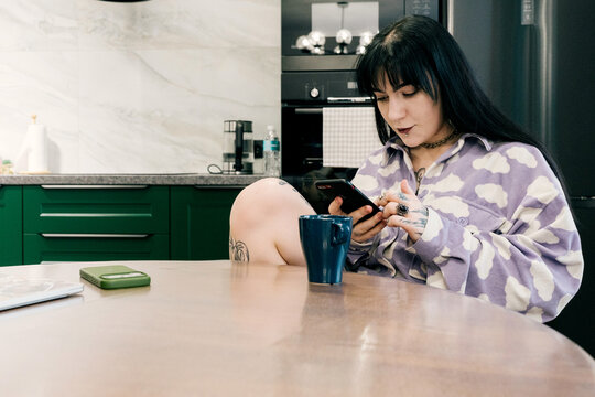 A woman is sitting in the kitchen with a smartphone in her hands.