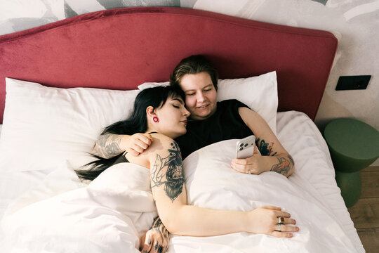 Girlfriends relax in bed, looking at the phone.