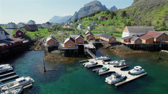 Picturesque aerial view revealing a traditional norwegian fishing village with rorbu cabins and boats moored in the clear water of a fjord
