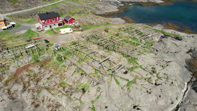 Breathtaking aerial footage flying over traditional wooden racks used for drying codfish, next to a typical red house on the coast