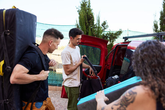 Friends prepare climbing gear at a parking area under sunlight