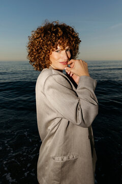 Woman with curly hair looking at camera by the sea