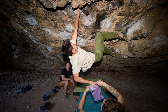Climber works on bouldering problem in cave at night
