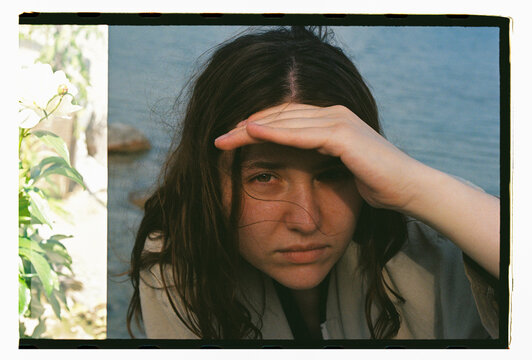 A woman shields her eyes by the water's edge