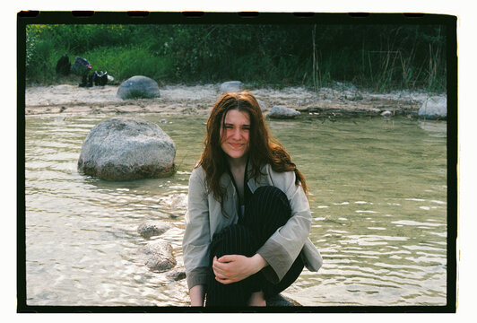 A young woman sits smiling on a rock in a shallow river