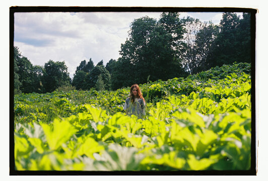 A woman stands deep in a lush green field of wild plants