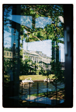 A summer park and neoclassical facade glimpsed through iron railings