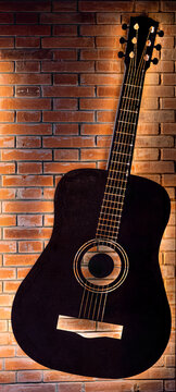 a acoustic guitar finished in solid black, featuring a traditional six-string configuration and a standard light-colored acoustic bridge on brown brick textured wallpaper