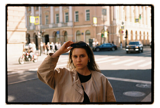 A young woman holds her sunglasses on a busy city street