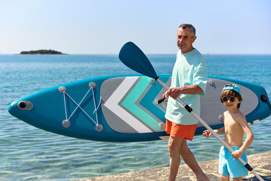 Father and Son Carrying Paddle Board by the Sea