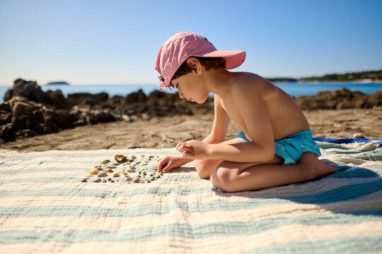 Child Sorting Seashells on a Beach Blanket
