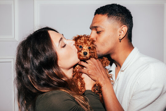 Young couple with their cute brown puppy sharing a kiss