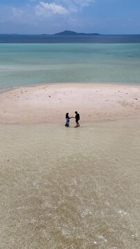 A couple walks along the white sandy beach at Kerayaan Beccu Beach and smiles at the camera
