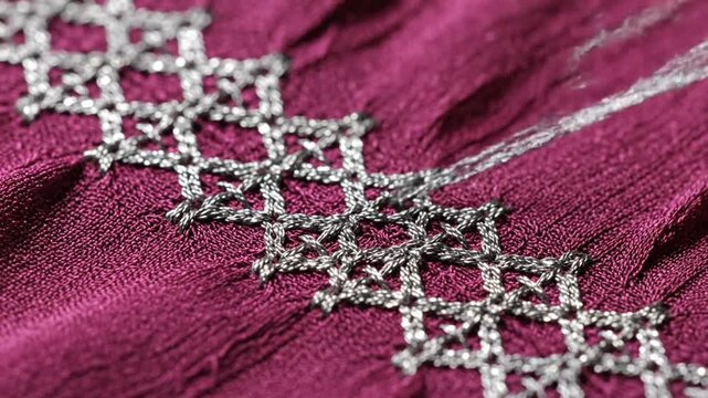 Silver embroidery pattern on burgundy fabric with a needle