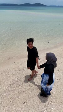 A couple walks along the white sandy beach at Kerayaan Beccu Beach and smiles at the camera