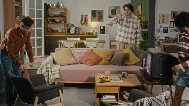 Multiethnic young adults hanging out in retro living room, laughing and playing with retro game controller. Footage suitable for youth lifestyle marketing and diverse friendship campaigns