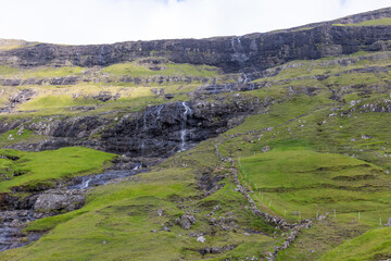 Fototapeta premium Waterfall Cascading Over Rugged Cliffs in Faroe Islands