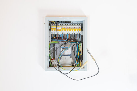 Open electrical distribution panel with circuit breakers and wiring installed on a white wall