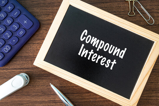Compound Interest text on black chalkboard with calculator and office supplies on wooden desk, finance and banking concept