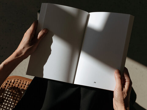 A Serene Moment with a Book: A person's hands gently hold open a blank book, bathed in soft sunlight casting dramatic shadows, suggesting a moment of quiet contemplation or learning.