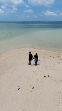 A couple walks along the white sandy beach at Kerayaan Beccu Beach and smiles at the camera