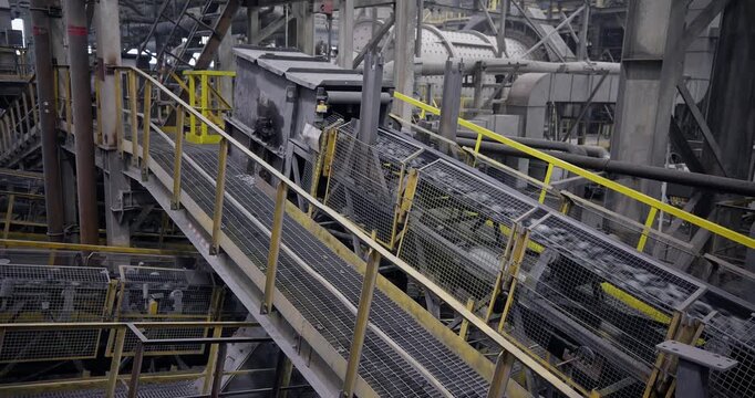 Conveyor belt with ore moving along inclined metal walkway inside industrial processing plant. Concentration factory for copper, gold, magnetite concentrate.