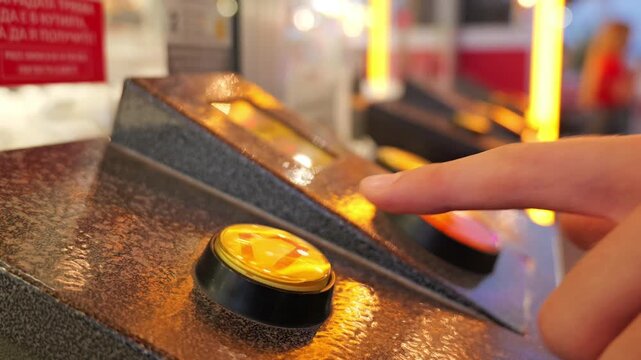 Person pressing illuminated yellow button on arcade game console