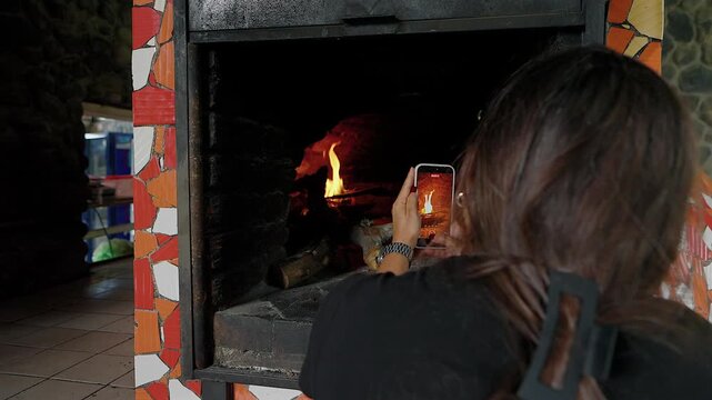 person recording video of wood fire inside brick oven with smartphone