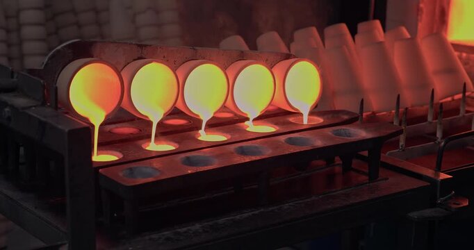 Slow motion close up of molten gold, copper metal pouring from crucibles into molds inside industrial foundry near glowing furnace in Concentration factory.