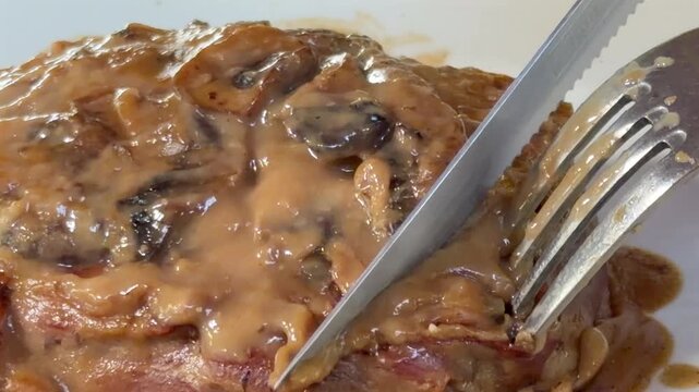 slicing a juicy filet mignon cooked meat dish with mushroom gravy using fork and knife