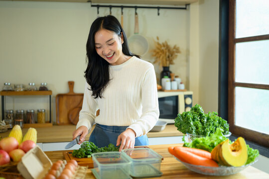 Young Woman Chopping Fresh Kale in a Modern Home Kitchen with Colorful Vegetables and Fruits
