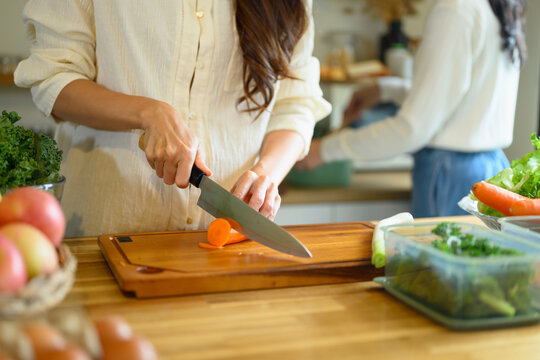 Woman Chopping Fresh Carrots on Wooden Cutting Board in Home Kitchen with Vegetables and Fruits