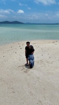 A couple walks along the white sandy beach at Kerayaan Beccu Beach and smiles at the camera