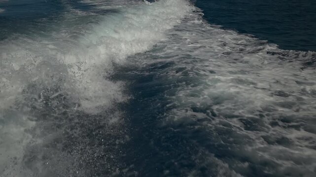 Turbulent white foam water trail behind a large boat in a calm blue sea on a sunny day, slow motion