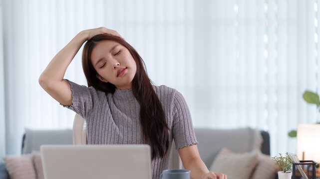 Young Asian woman experiencing headache and mental fatigue while working on laptop in bright home interior with copy space