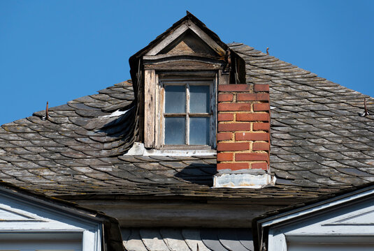 Weathered dormer window and brick chimney on a historic slate roof