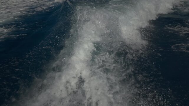 Turbulent white foam water trail behind a large boat in a calm blue sea on a sunny day, slow motion