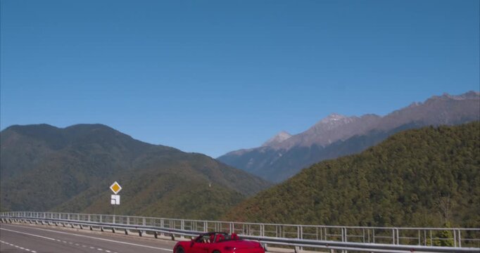 Side rear view of red convertible driving away on mountain highway