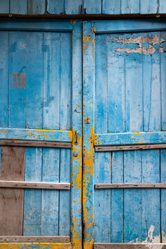 A rustic and weathered background of an old wooden double door featuring peeling blue paint, exposed yellow underlayers, wood grain, and vintage architectural charm, ideal for design backgrounds.