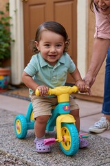 Fototapeta premium Toddler riding colorful tricycle with caregiver support outdoors