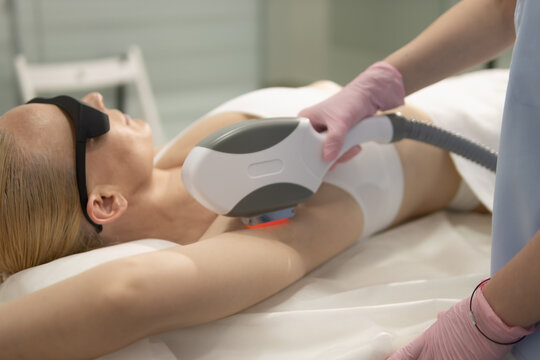 Woman receiving modern laser hair removal treatment from a beautician in medical uniform and protective gloves, achieving smooth skin and aesthetic body care results
