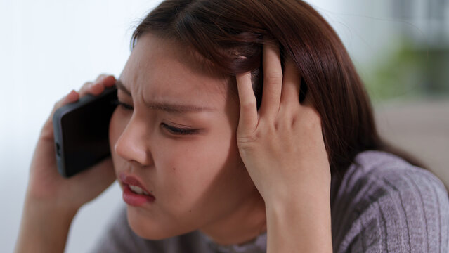 Stressed Asian woman holding phone to head experiencing frustration anxiety in bad mood at home
