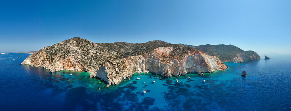Aerial view of Kleftiko Bay on Milos Island, Greece, showcasing dramatic white cliffs, turquoise water, and anchored boats beneath a clear summer sky &mdash; a stunning example of Aegean coastal beauty.