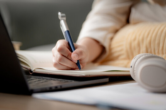 Online learning and homework study concept. Student writing notes while using a laptop at home, representing distance education, e-learning, self-study, online classes and academic success.